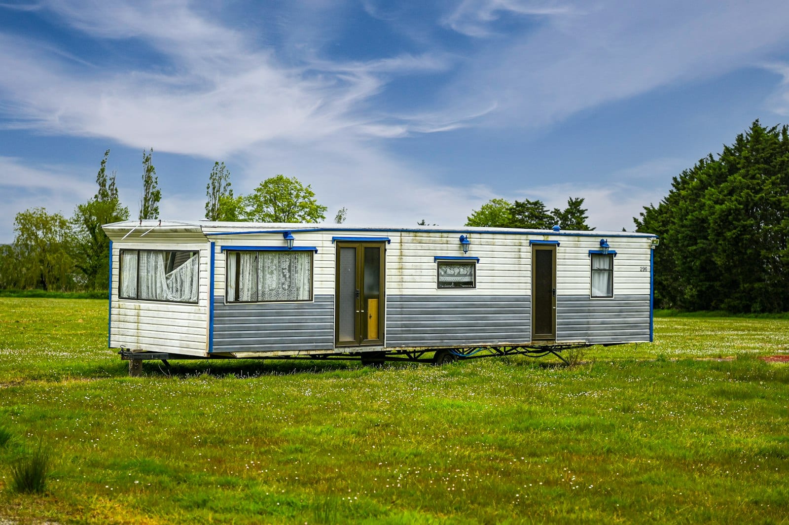 Single-wide mobile home on a grassy lot under a blue sky